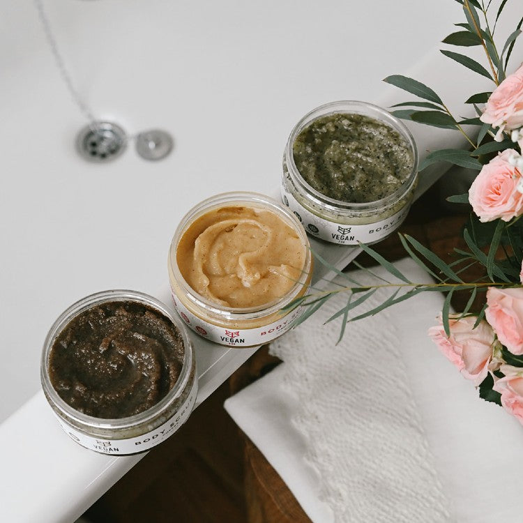Vegan Fox ginger anti-cellulite scrub jars in three colors placed on bathtub edge with flowers nearby