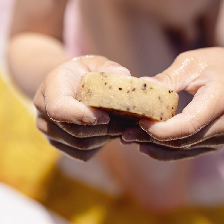 Close-up of hands holding a round kiwi seed body scrub bar with visible seeds