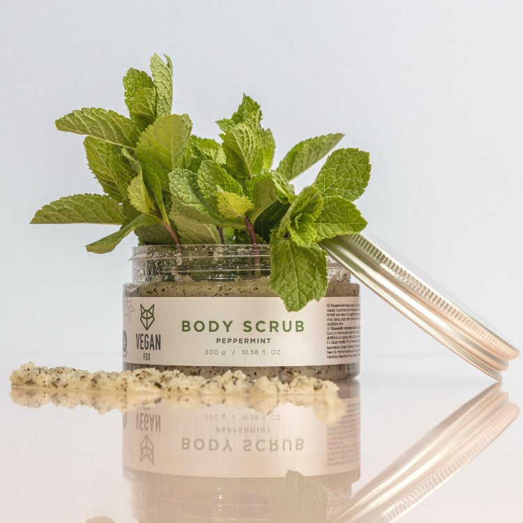 Vegan Fox peppermint body scrub jar with fresh peppermint leaves and exfoliating scrub on surface
