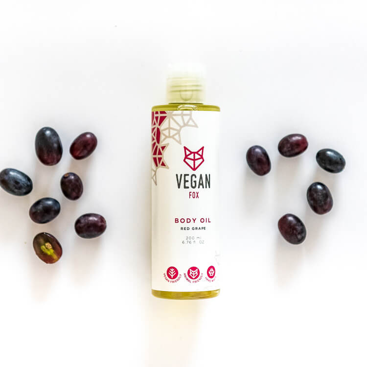 Vegan Fox red grape body oil bottle surrounded by fresh red grapes on white background